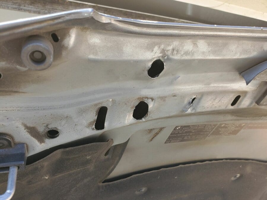 Multiple unnecessary holes drilled through a car panel by an inexperienced PDR technician, leaving open rust points