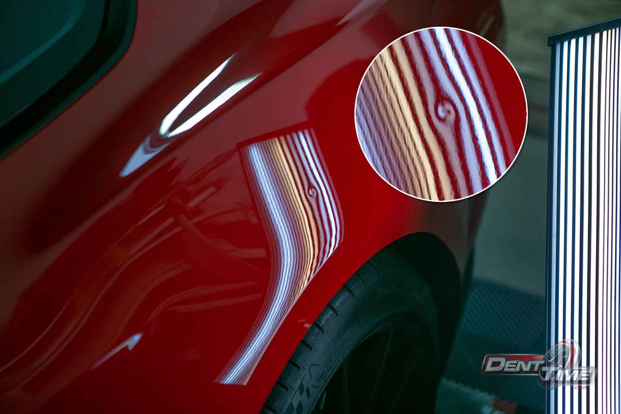 Dent bending the reflection-board lines on a red panel, before paintless dent repair in San Diego
