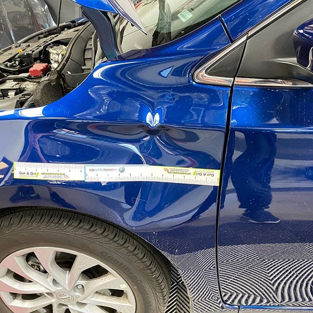 Body line dent on a blue fender measured during advanced paintless dent repair training