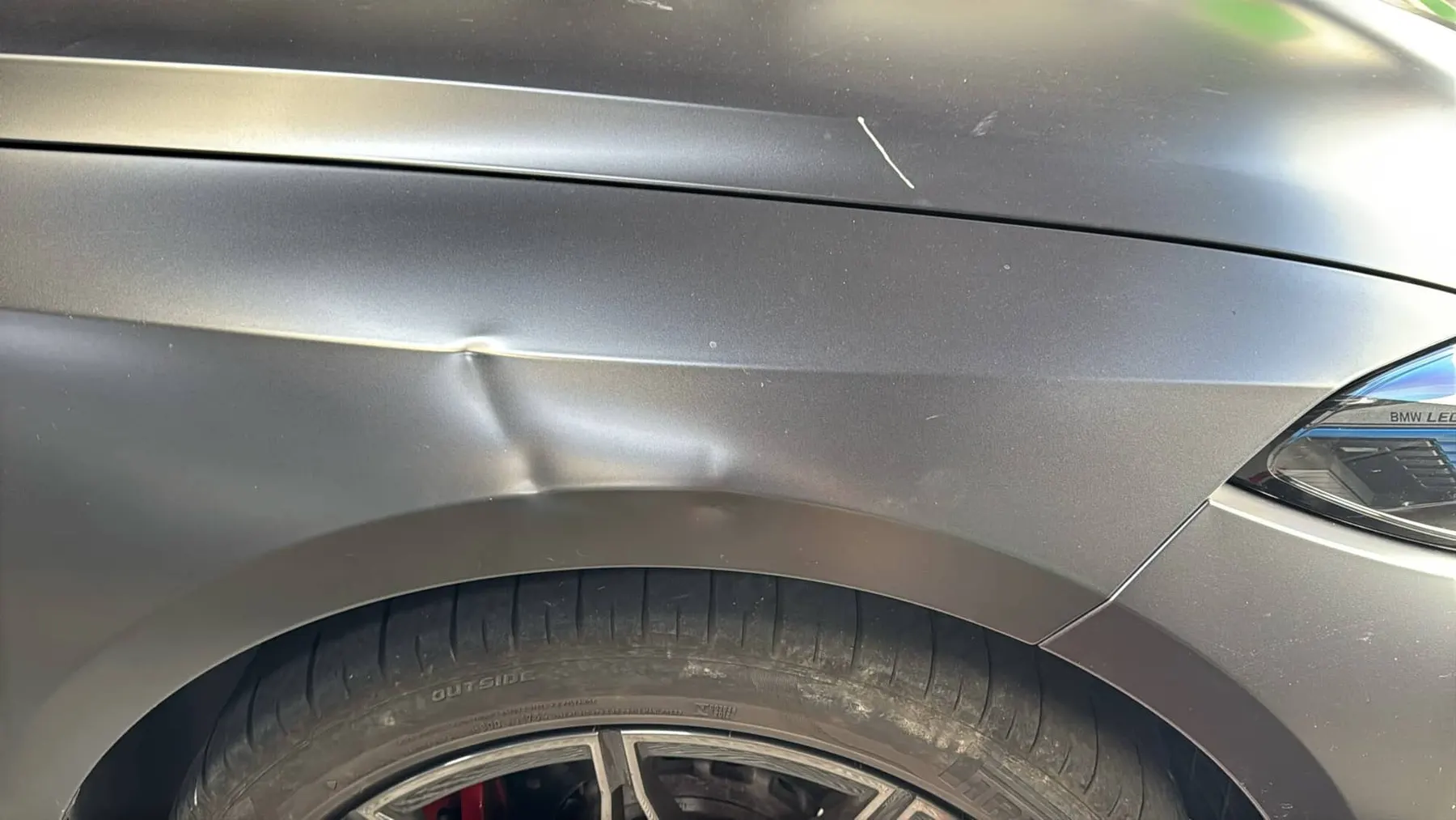 Matte BMW fender with a sharp crease dented into the body line before paintless dent repair