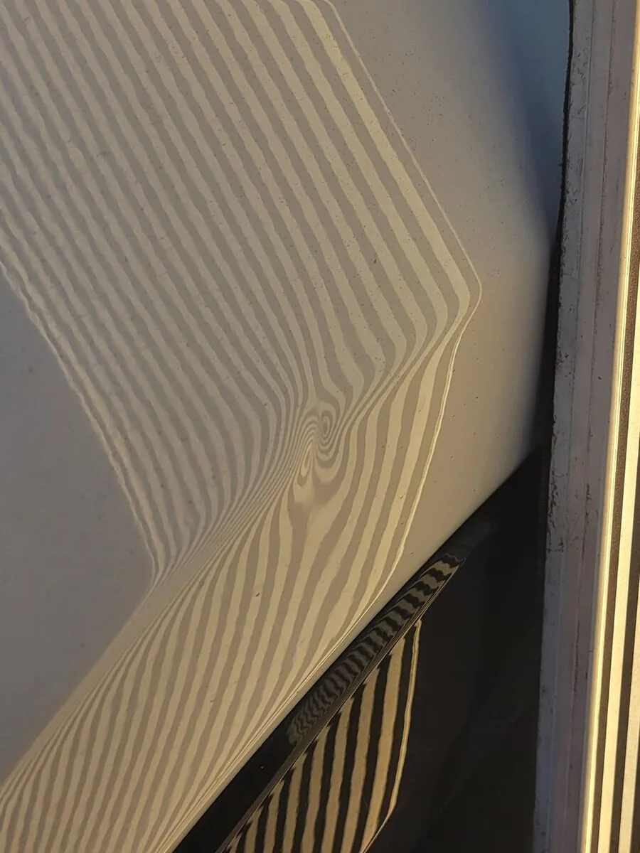 A line board reflected in a car door before repair. The straight lines twist and knot where the dent is.