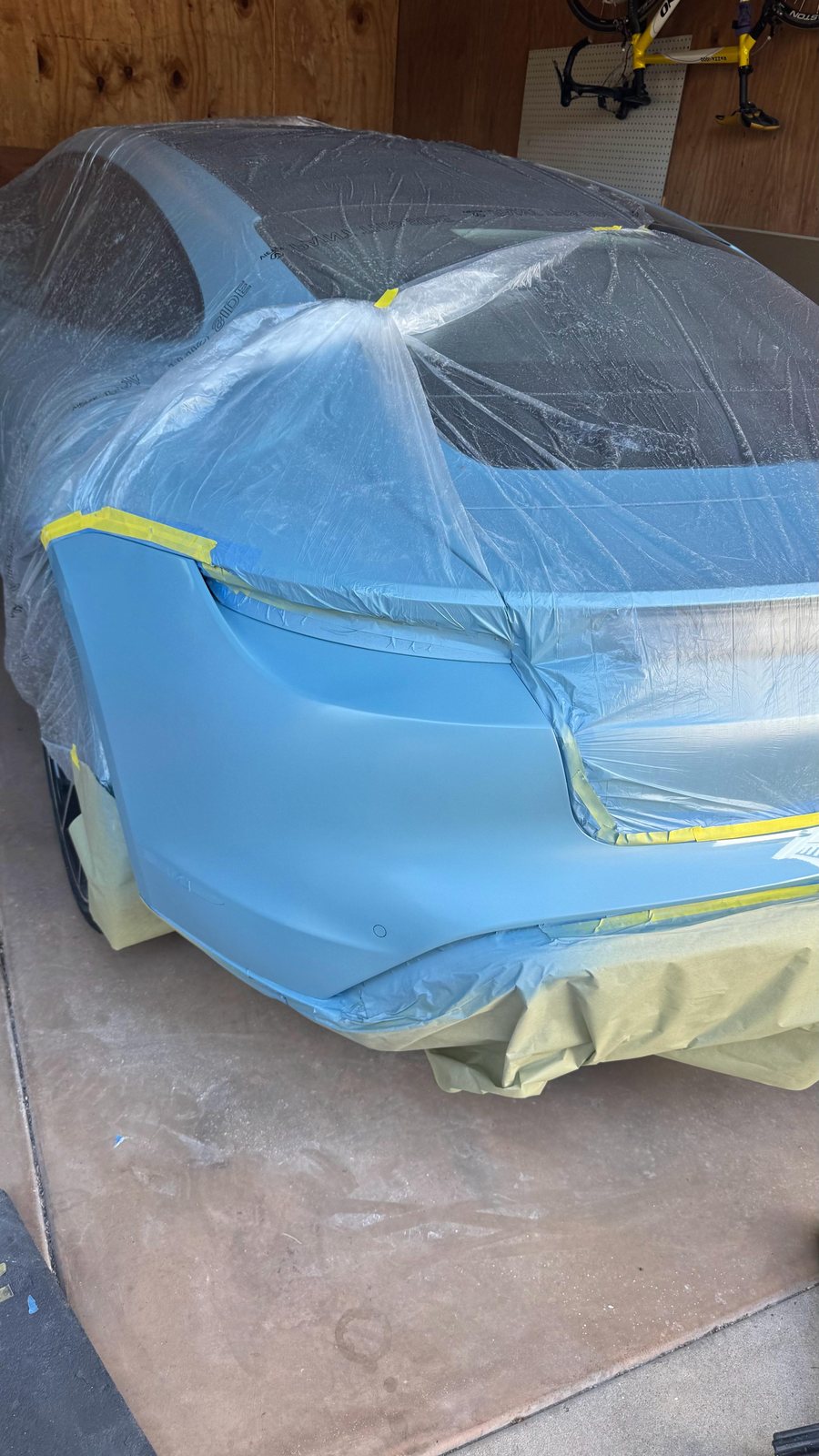 Porsche Taycan masked and sheeted for a mobile bumper refinish in a San Diego garage