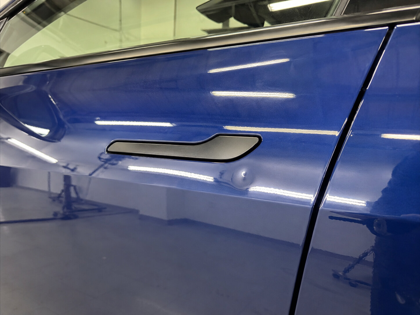 Dent in the aluminum door of a blue Tesla before paintless dent repair