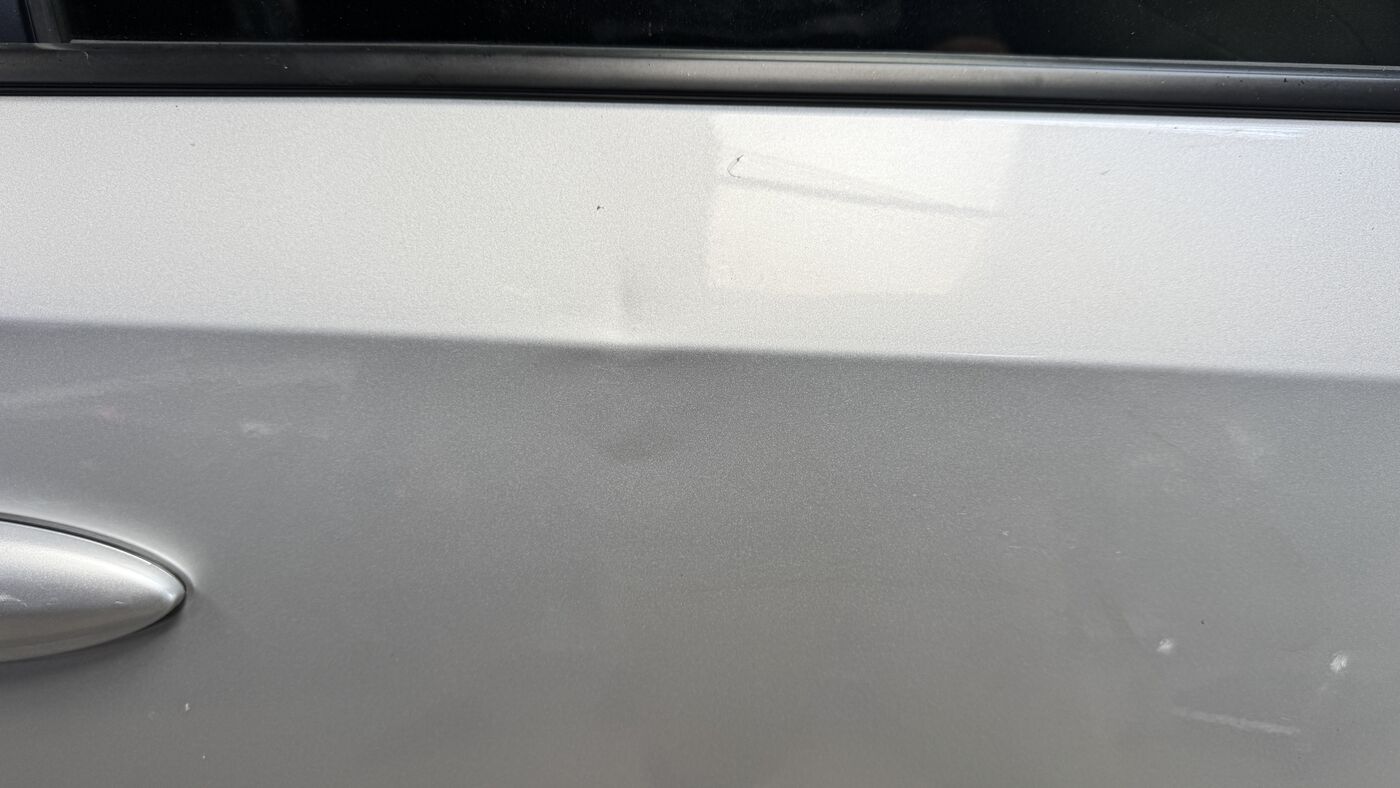 Silver door panel after an Improvement level paintless dent repair, damage substantially reduced